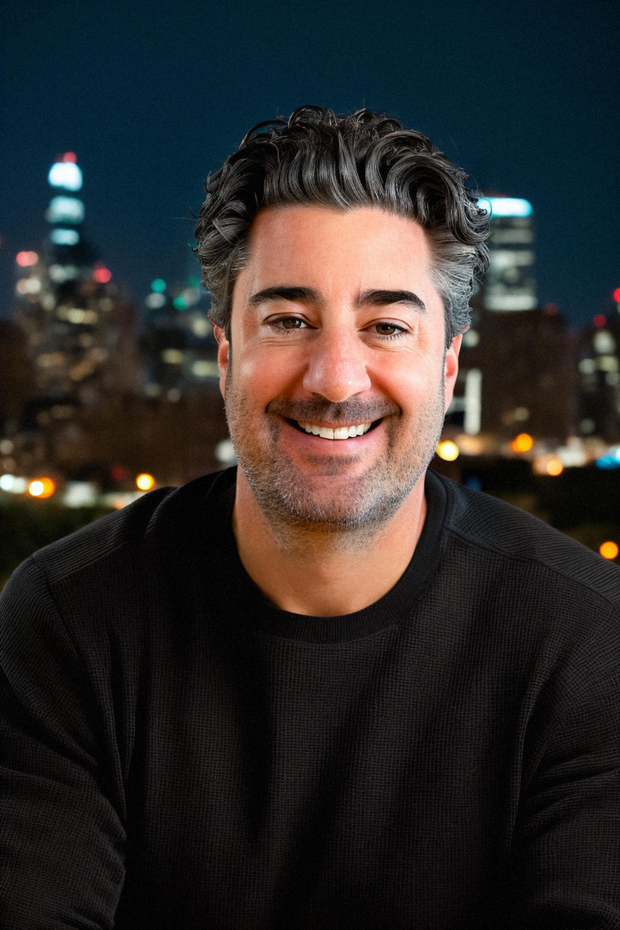 Jay Schwedelson smiling, with a city skyline at night behind him